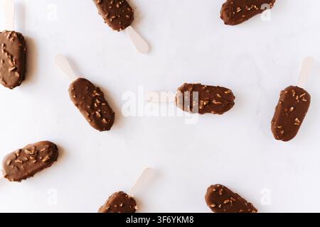 Chocolate coated ice cream bars with nuts arranged on a white background. Flat lay. Top view Stock Photo
