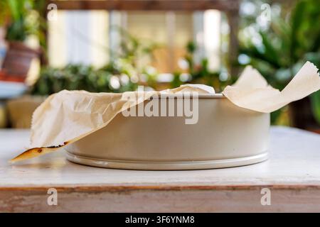 Low side view of a round springform baking pan lined with crumpled parchment paper on a table on a summer balcony. Blurred background Stock Photo