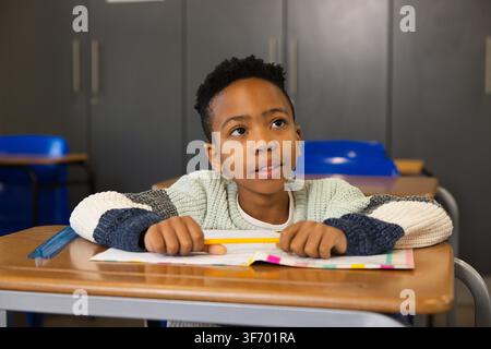 African American boy sitting at school desk holding yellow pencil, using open book and clear ruler. Classroom, student, focus, study, learning, organi Stock Photo
