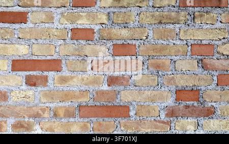 Rustic brick wall with yellow and red bricks on concrete External wall covering. Full frame, background and texture. Stock Photo
