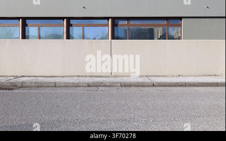 Cream colored plaster fence with gray modern building with storefronts behind. Concrete sidewalk and street in front. Background for copy space. Stock Photo