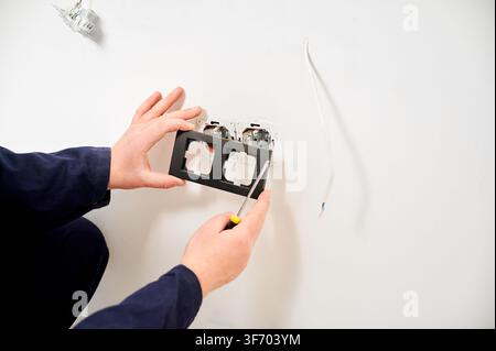 Electrician aligning socket cover and checking wall outlets with tool. Close view of finishing stage in electrical installation, renovation and maintenance concept Stock Photo
