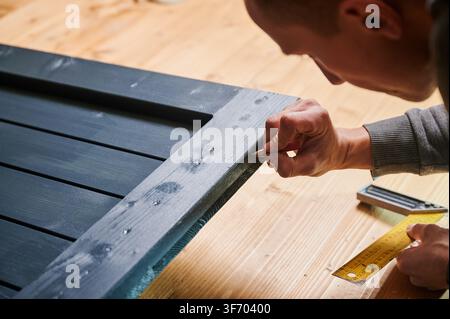 Man marking wooden door frame with pencil, close up of hands during carpentry work. Indoor workshop with ruler and square on wooden floor, furniture assembly and precision fitting concept Stock Photo