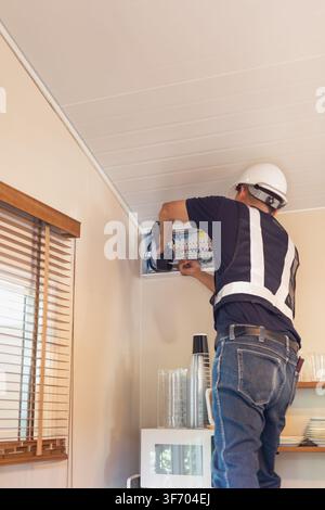 Electrician wearing a hard hat using a digital clamp meter to measure electric in breaker panel Stock Photo