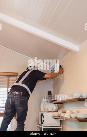 Technician wearing a hard hat inspecting a wall mounted electrical control panel Stock Photo