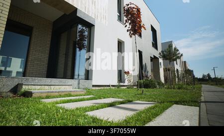 Row of modern townhouses featuring minimalist design, green lawn, concrete path, and clear blue sky Stock Photo