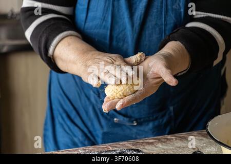 Mature hands form soft dough balls for traditional syrniki, capturing the authentic process of making delicious dairy pancakes with a rustic and artis Stock Photo