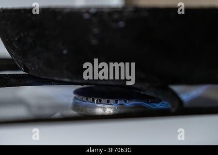 Black frying pan sitting over a glowing blue flame on a gas range, highlighting the culinary heat and energy used to cook dough cakes while evoking a Stock Photo
