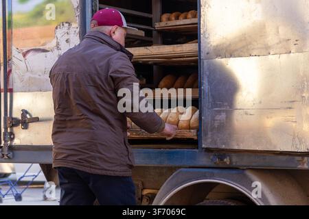 An employee in a jacket unloads freshly baked bread from a transport vehicle for delivery to illustrate the logistics of food supply chains and reliab Stock Photo