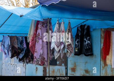 Various fabric accessories and floral headscarves hang under a blue tarp at a market stand, showcasing traditional craftsmanship and retail culture wi Stock Photo