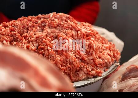 Close-up of raw minced meat piled in a metallic container at a bustling butcher shop, highlighting culinary preparation, grocery trade, and essential Stock Photo
