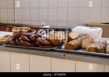 Assorted smoked pork products and coiled sausages displayed on stainless steel trays in a butcher shop, emphasizing natural craft, food processing, an Stock Photo