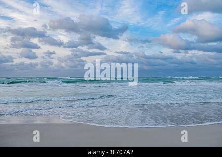 Waves crash on the shore under a cloudy sky at twilight on a beach. Stock Photo