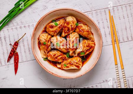 Delicious dumplings served in a bowl with a spicy sauce and green onions on wooden table Stock Photo