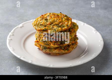 Stack of Homemade Zucchini Fritters (Mucver) on a Plate with Fresh Tomatoes, Mint and Olive Oil Stock Photo