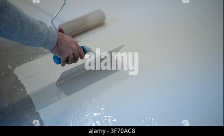 Worker Applying White Liquid Floor Coating With Roller and Trowel Stock Photo