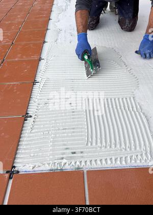 Worker Spreading Tile Mortar Beside Newly Laid Ceramic Tiles Stock Photo