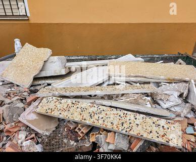 A container holds a mix of broken terrazzo tiles and concrete rubble from house renovation work in an outdoor setting. The area shows signs of ongoing Stock Photo