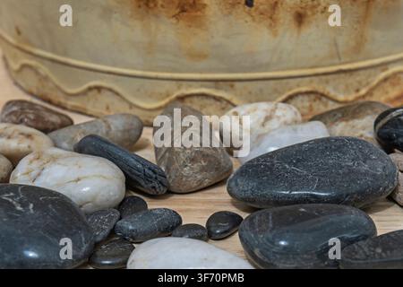 Polished Black and White River Stones on Wood Surface Beside Rustic Weathered Metal Tub Stock Photo