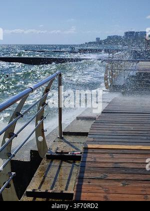 Large wave hitting wooden pier jetty with a lot of splashes on a sunny day. Storm, stormy sea. Weather. Travel, tourism,vacation. Coast, coastal, shore Stock Photo