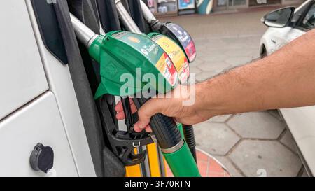 Deutschland, Europa. Detailaufnahme einer Hand, die eine grüne Shell FuelSave Super E10 Zapfpistole aus der Halterung einer Zapfsäule entnimmt. Im Hintergrund sind weitere Kraftstoffsorten sowie ein geparkter Pkw an der Tankstelle zu sehen. Symbolfoto zu Tanken, Kraftstoffversorgung, Mobilität, Energie, Autofahren und Verbrauch. *** Germany, Europe: Close-up of a hand removing a green Shell FuelSave Super E10 fuel nozzle from the holder on a gas pump. In the background, other types of fuel and a parked car at the gas station are visible. Stock photo illustrating refueling, fuel supply, mobilit Stock Photo