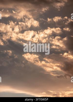 Golden light breaks through dramatic clouds at sunset. Clouds glow with warm amber and soft gray tones. Sunlight creates rays through cloud cover Stock Photo