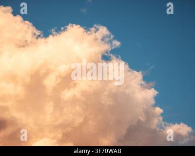 Large, fluffy cloud with golden edges against clear blue sky. Warm sunlight highlights cloud's textured surface Stock Photo