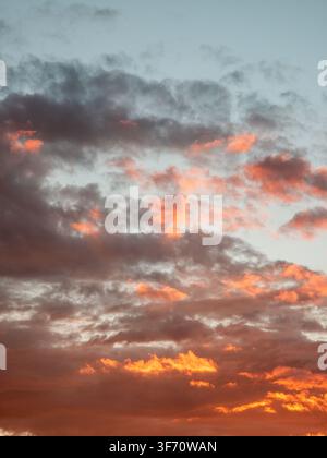 Sky at dusk with clouds painted in orange and gray tones. Clouds scattered across the horizon. Warm sunset colors glow through thin cloud layers Stock Photo