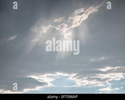 Sunlight breaks through gray clouds in dramatic rays. Sky scene with soft, diffused light filtering between cloud layers Stock Photo