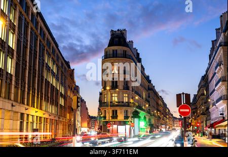 Evening view of a classic Paris street intersection featuring illuminated Haussmann architecture, light trails, and a twilight sky. Stock Photo