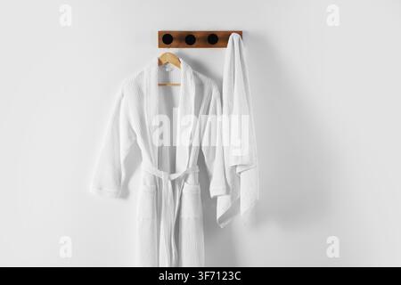 Clean cotton bathrobe and towel on white wall Stock Photo