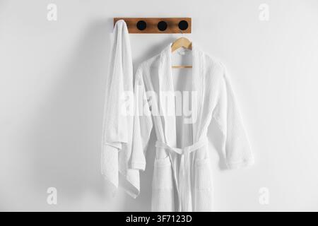 Clean cotton bathrobe and towel on white wall Stock Photo