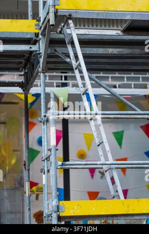 Modular steel scaffolding structure with internal access ladder, safety guardrails, and yellow wooden toe boards during building restoration Stock Photo