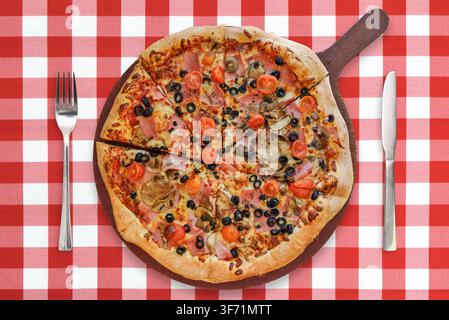 Traditional italian pizza with: ham, mushrooms, cherry tomatoes, mozzarella, black olives on a wooden board with cutlery on the background of red chec Stock Photo