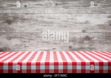 Italian cooking template - blank table with a red checked tablecloth on the blurred wooden vintage panels background. Stock Photo