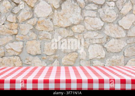 Italian cooking template - blank table with a red checked tablecloth on a old rustic stone wall background with copy space. Stock Photo