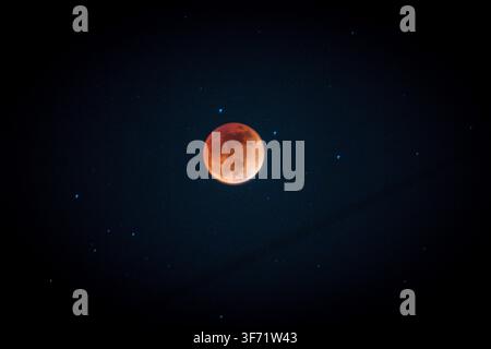 A deep orange-red blood moon glows during a total lunar eclipse, surrounded by faint stars in a dark night sky. Stock Photo