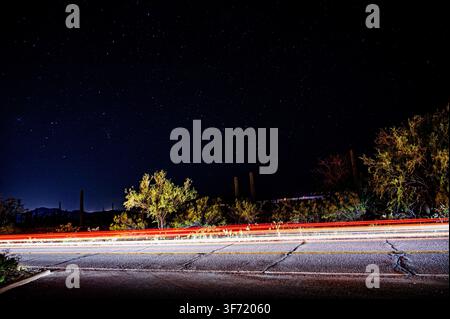 Long exposure captures a starry night sky and streaking vehicle light trails along a desert road in Arizona. Stock Photo