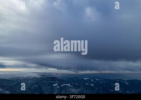 Aerial view of the snow-covered Black Forest landscape near Mummelsee with dramatic dark storm clouds gathering over the mountain peaks in Seebach, Ba Stock Photo