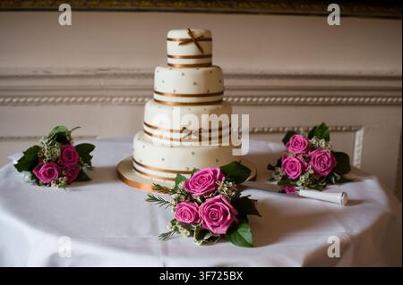 A four-tier wedding cake with bronze ribbons and rose bouquets displayed during a celebration at a grand, historic wedding estate. Stock Photo