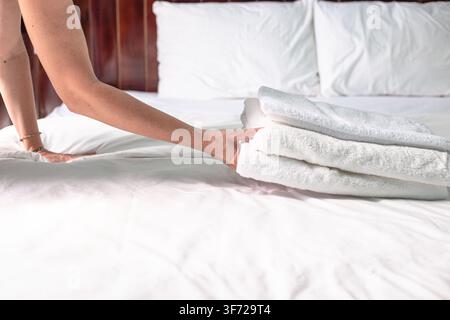 Housekeeper placing neat folded white towels on a freshly made hotel bed. Hospitality industry, room service, clean bedroom interior. Stock Photo