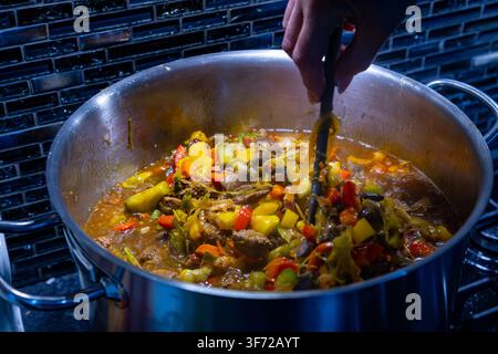 Homemade beef and vegetable stew simmering in a large pot on a kitchen stove Stock Photo