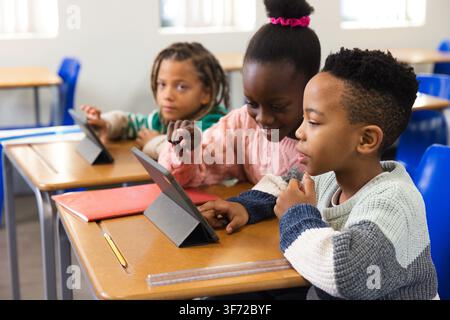 School-age students collaborating on tablets at classroom desks, pointing and tapping screens. Pupils, devices, learning, collaboration, teamwork, dig Stock Photo