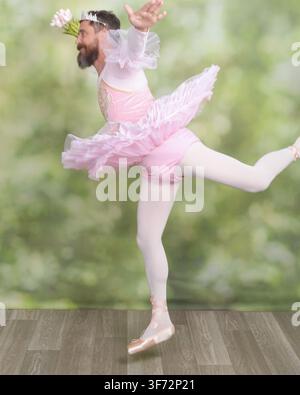 Bearded adult man wearing a pink tutu, tiara and pointe shoes performs an energetic grand leap in a humorous studio ballet portrait. Stock Photo