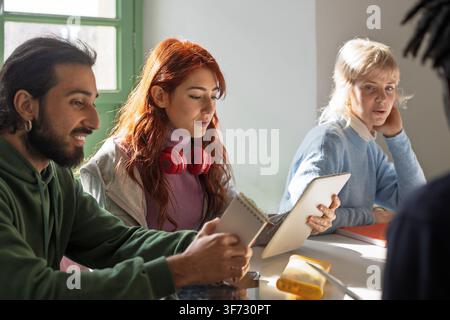 Group of diverse university students attending a classroom discussion while using notebooks and digital devices. Authentic academic environment showin Stock Photo