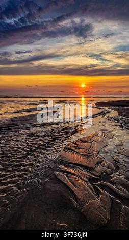 Golden sunset over the ocean coast with dramatic cloudy sky and wet sandy textures. Stock Photo