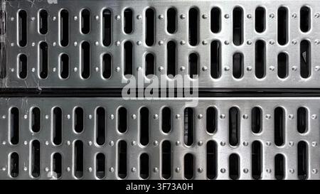 Close-up of perforated metal grate texture with repeating industrial pattern and dark openings. Stock Photo