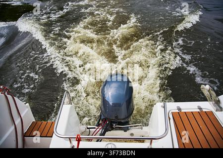 Trail of water behind a fast motorboat on the lake. Dynamic wake left by an outboard boat engine. Close up of the rear deck and motor of a pleasure bo Stock Photo