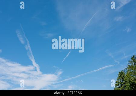 Bright blue sky with thin white clouds and multiple airplane contrails on a sunny summer day Stock Photo