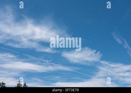 Blue summer sky with white cirrus clouds and long airplane contrails. Stock Photo